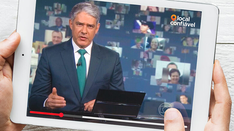 Pessoa segurando o tablet com o vídeo da reportagem, Willian Bonner na bancada do Jornal Nacional