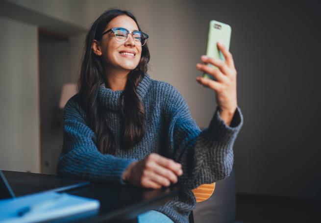 menina sorrindo segurando e olhando para o celular na mão